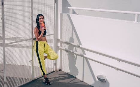 Fashionable woman in workout attire enjoying an ice cream outdoors against a minimalist white background.