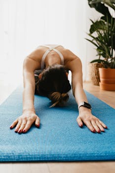 A woman practicing yoga in child’s pose on a blue mat indoors, promoting wellness and relaxation.